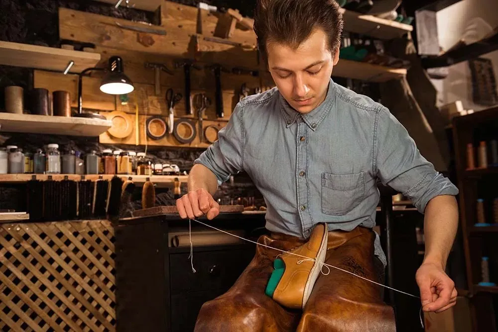 Zapatero cosiendo a mano un zapato con hilo en su taller